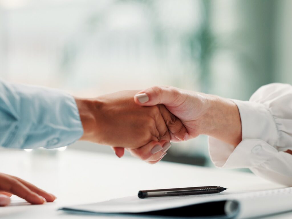 Sealing the Deal with a Handshake A handshake over a desk with a contract and pen marks a completed agreement.